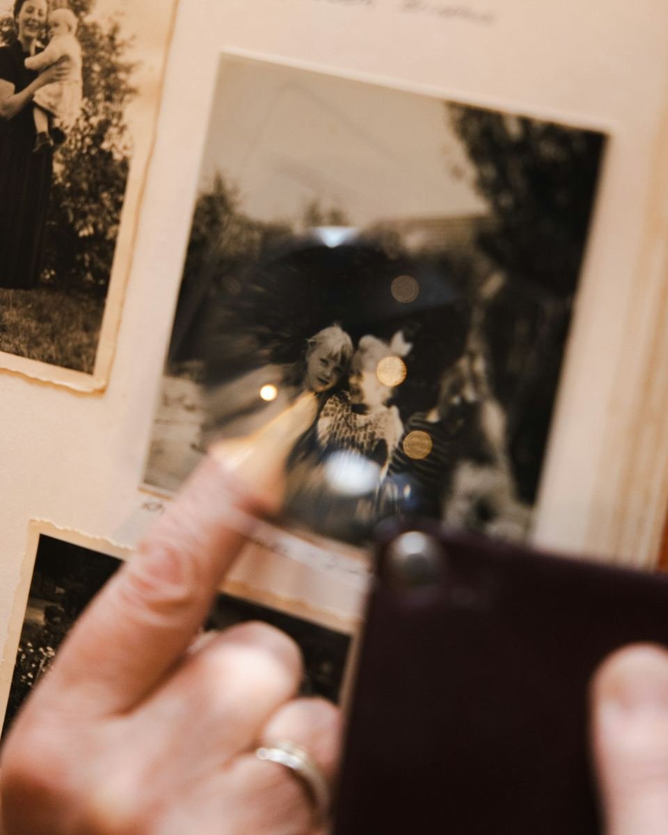 Manos examinando con una lupa un álbum de fotografías familiares antiguas