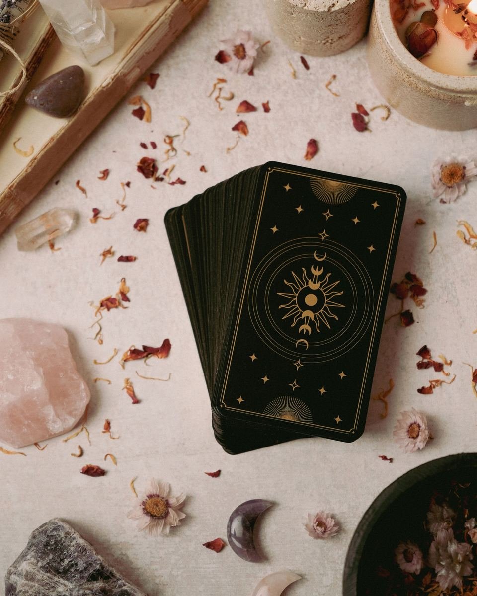 Mazo de tarot boca abajo con diseño de sol y luna, entre cuarzo rosado y flores secas