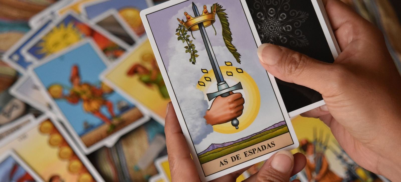 Manos sosteniendo la carta As de Espadas frente a una tirada de tarot