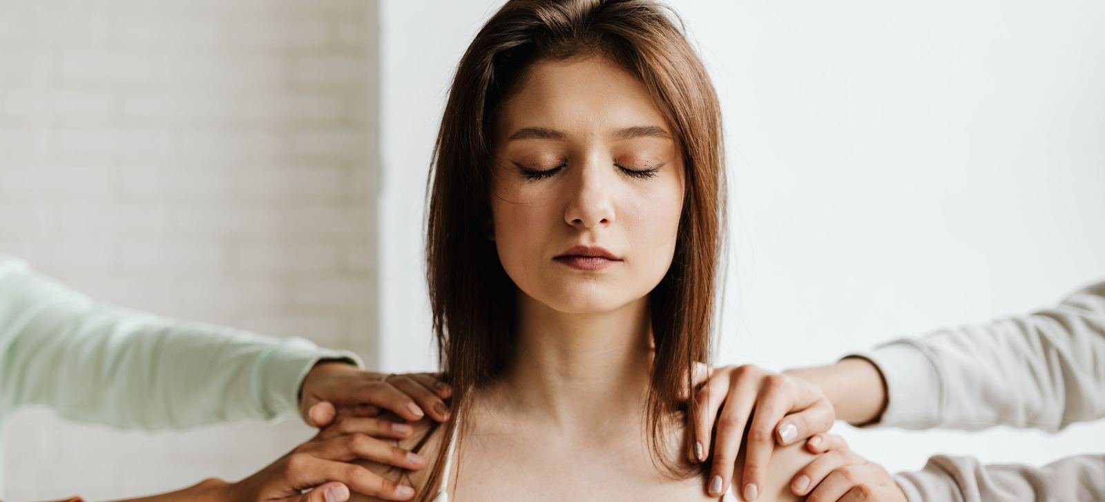 Mujer con los ojos cerrados recibiendo el apoyo de unas manos sobre sus hombros